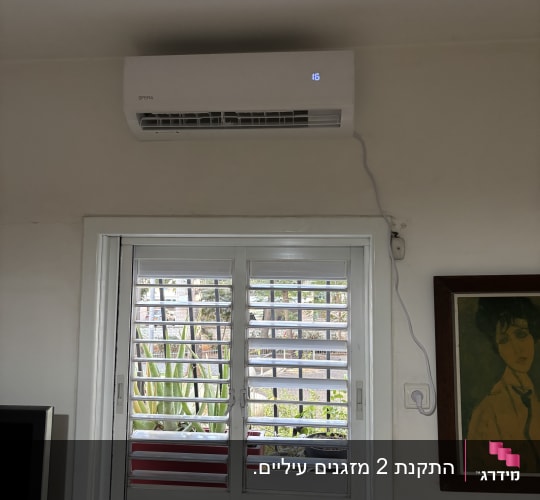 מזגן מותקן מעל חלון עם תריסים